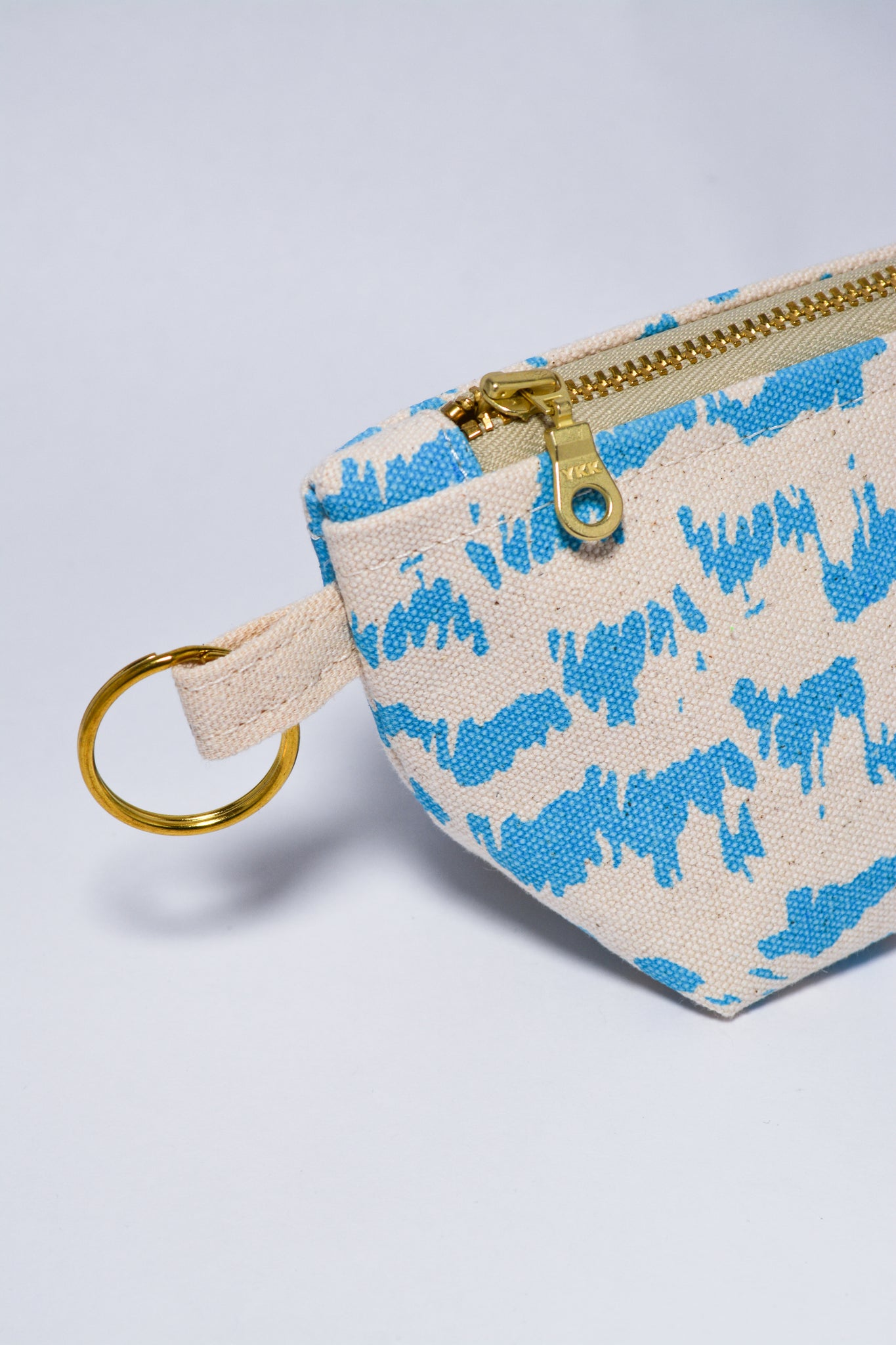 Small pouch with blue animal print pattern and gold zipper on a light gray background