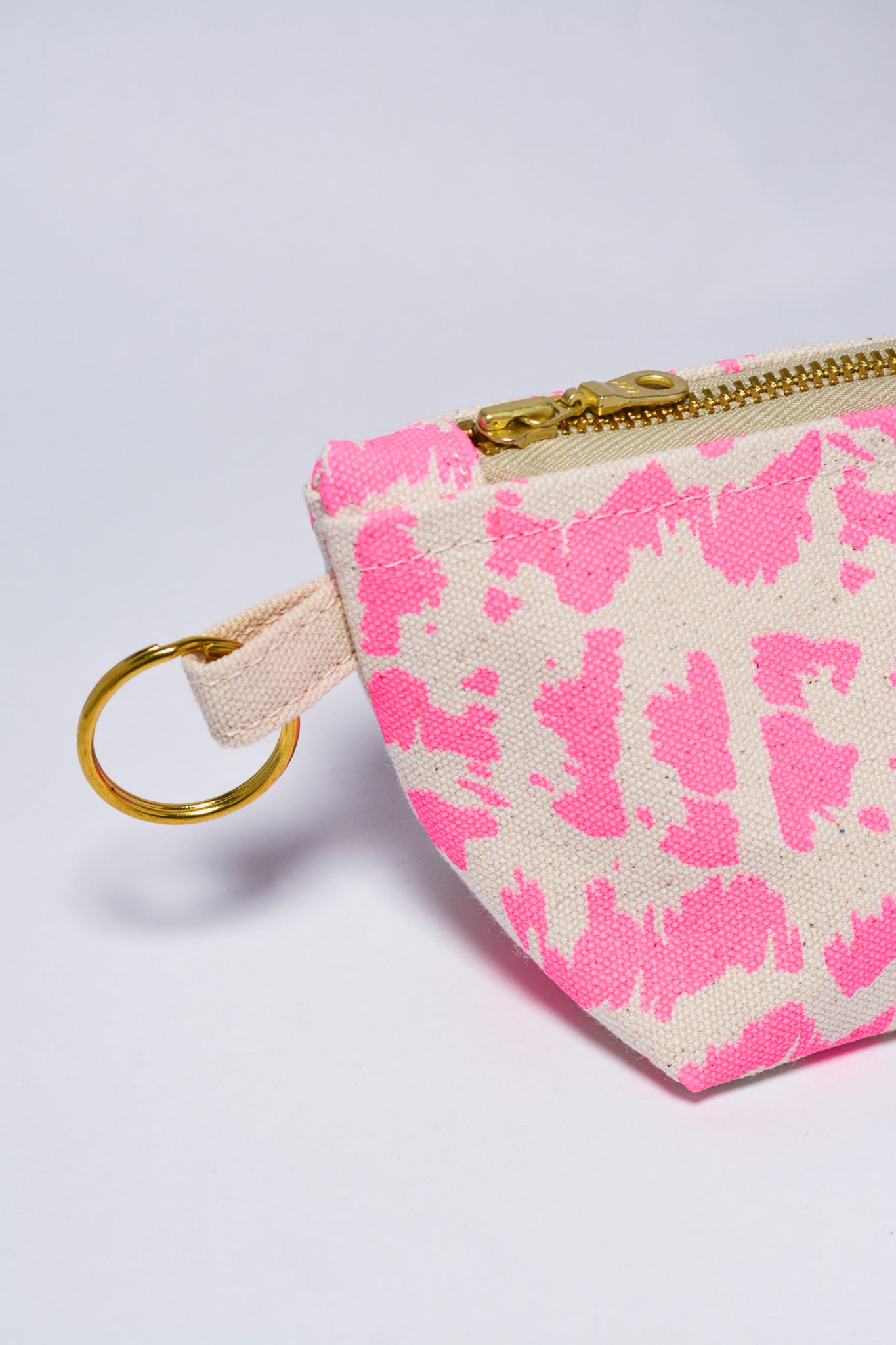 Small pouch with pink abstract pattern and gold zipper on a light gray background