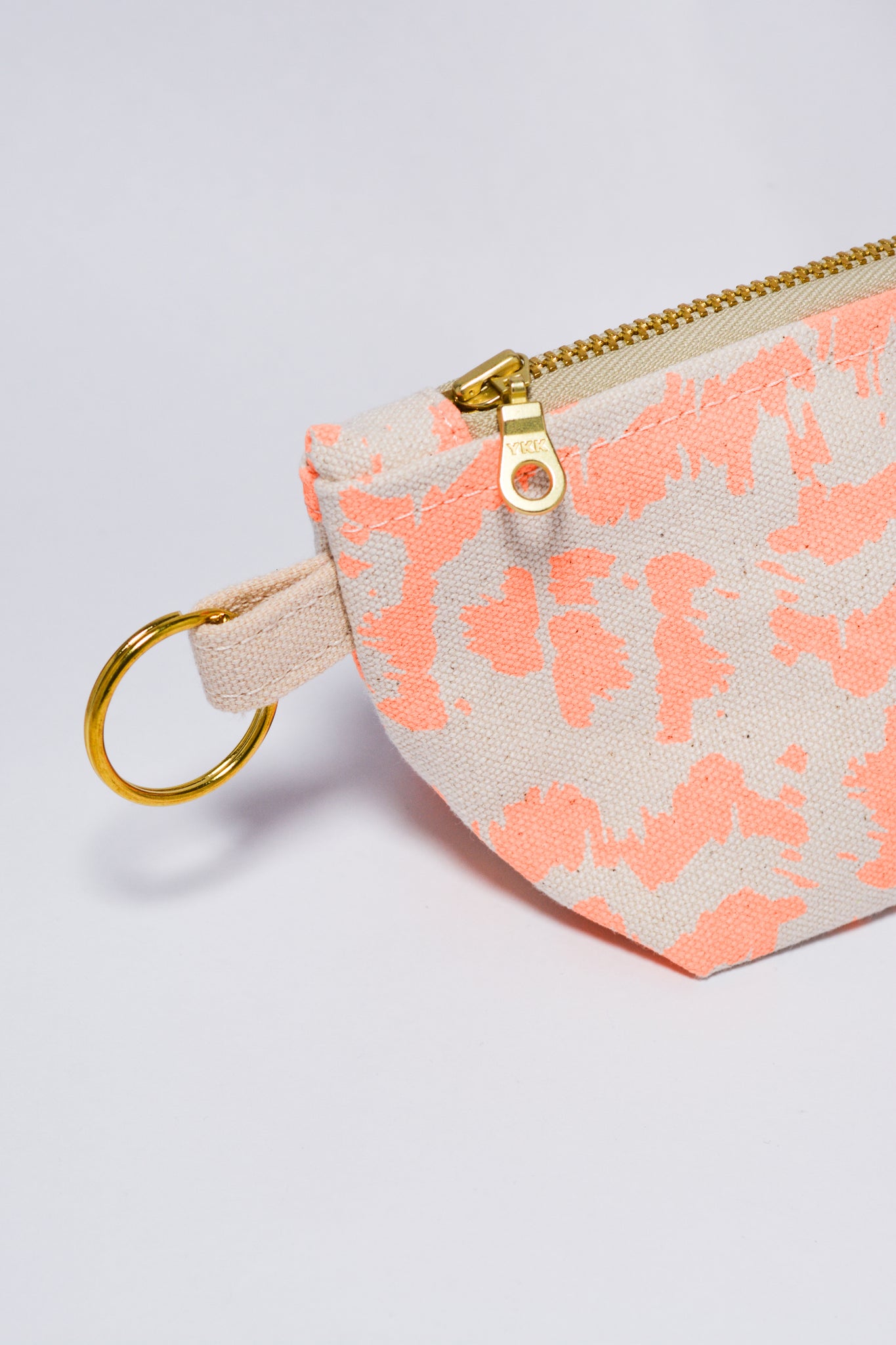 Small pouch with orange pattern and gold zipper on a light gray background