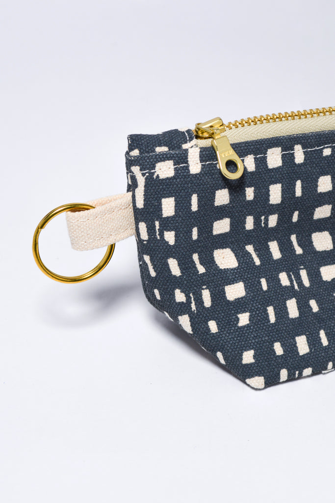 Small fabric pouch with geometric pattern and gold zipper on a light gray background