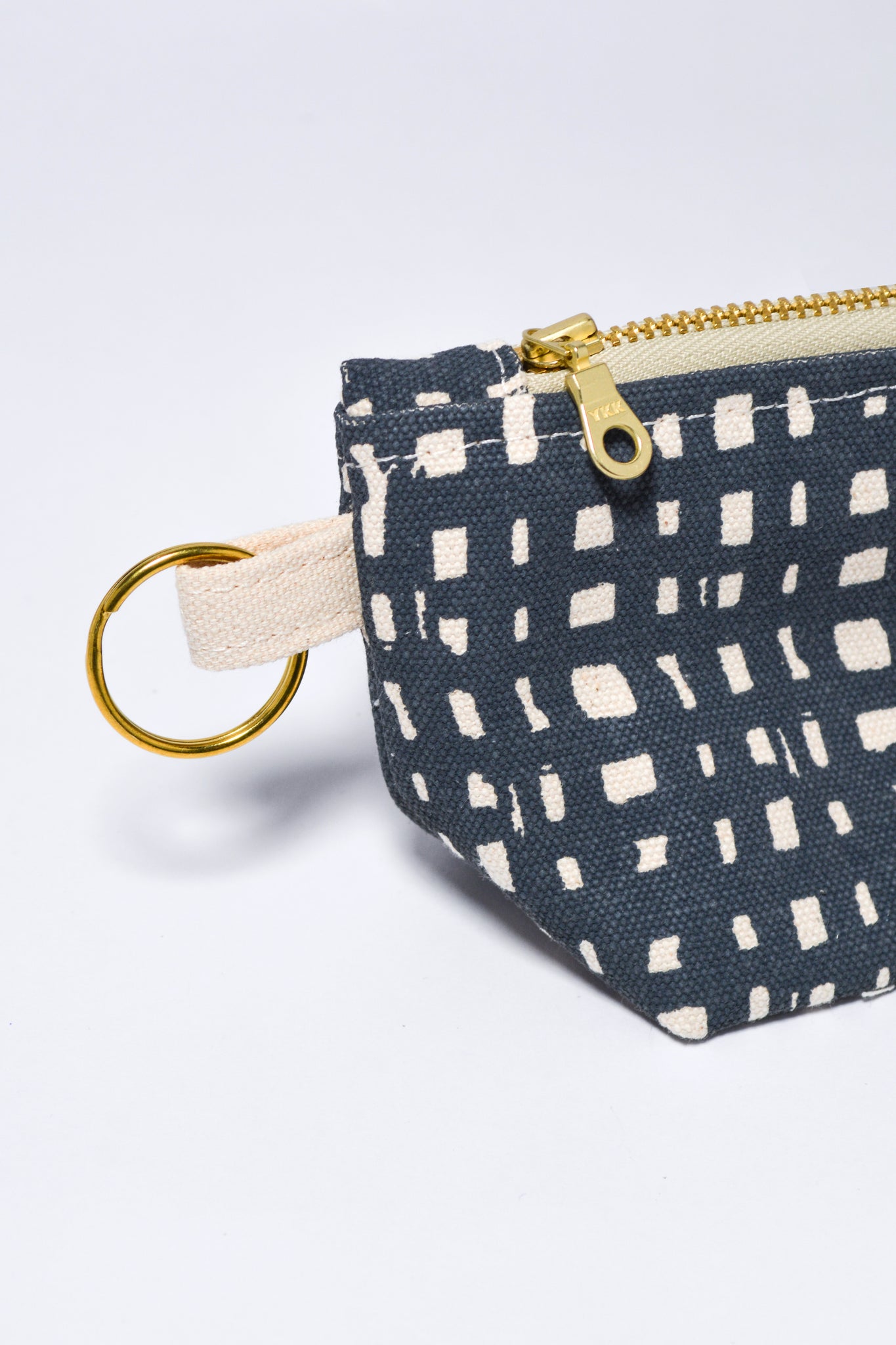 Small fabric pouch with geometric pattern and gold zipper on a light gray background